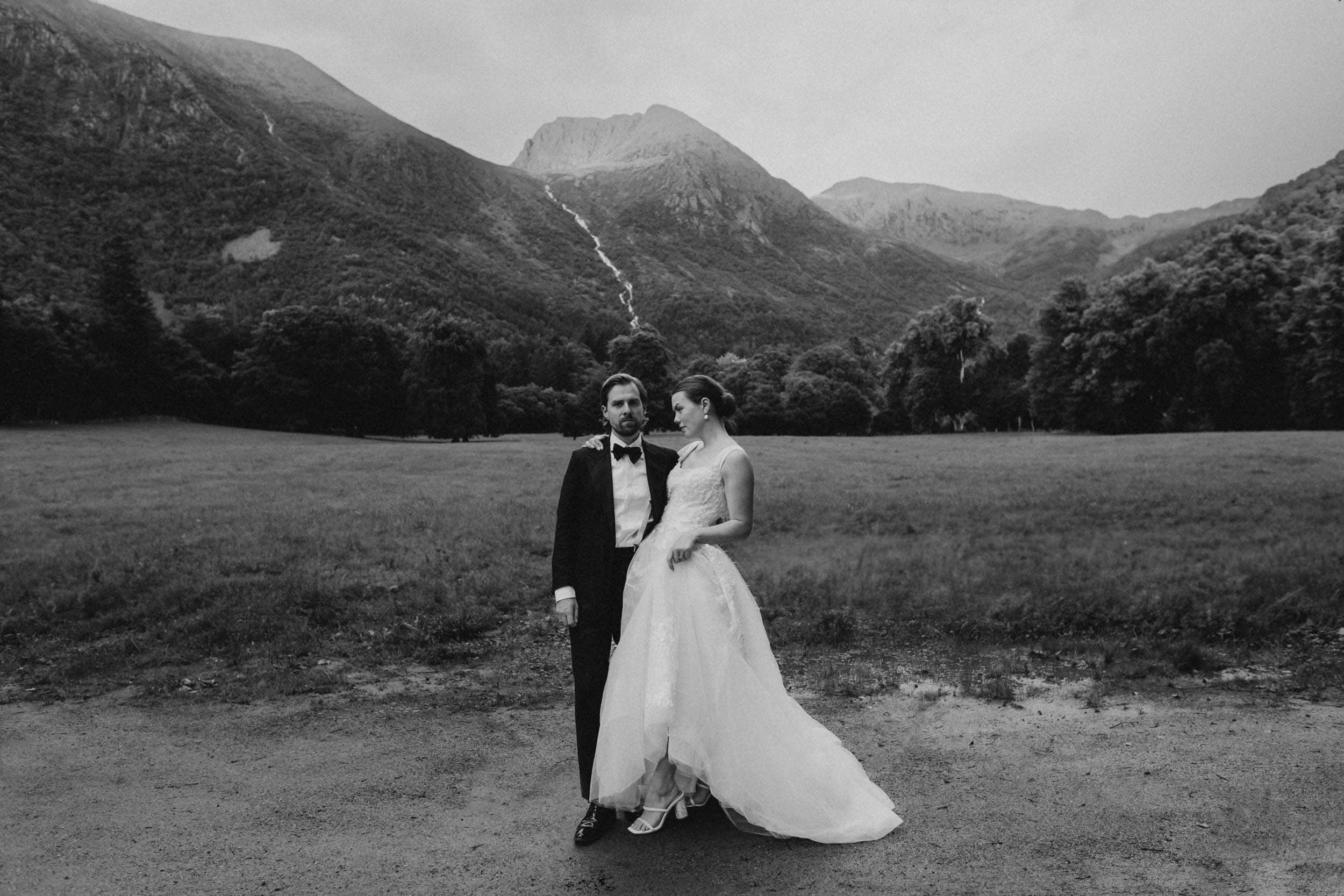 et brudepar som står mot store fjell og foss