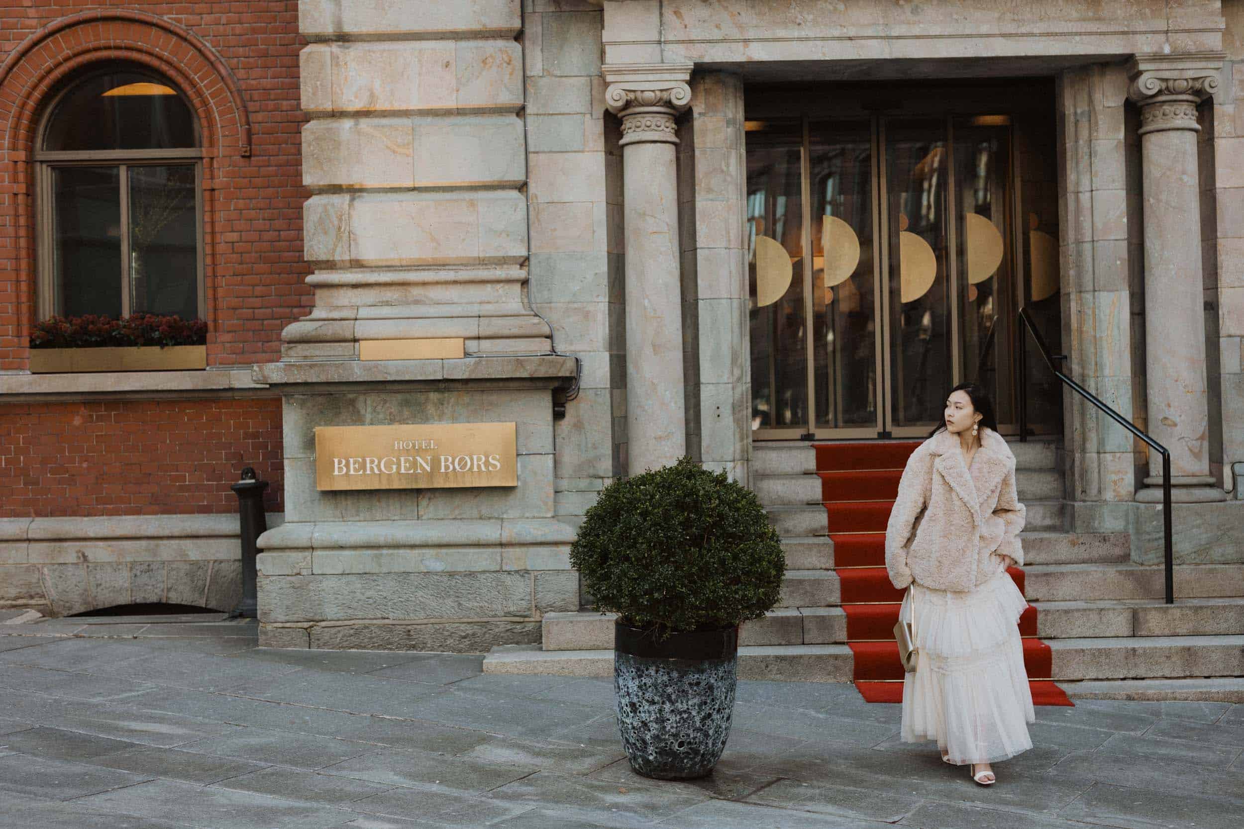 kvinne i hvit kjole går på rød løype utenfor et hotell