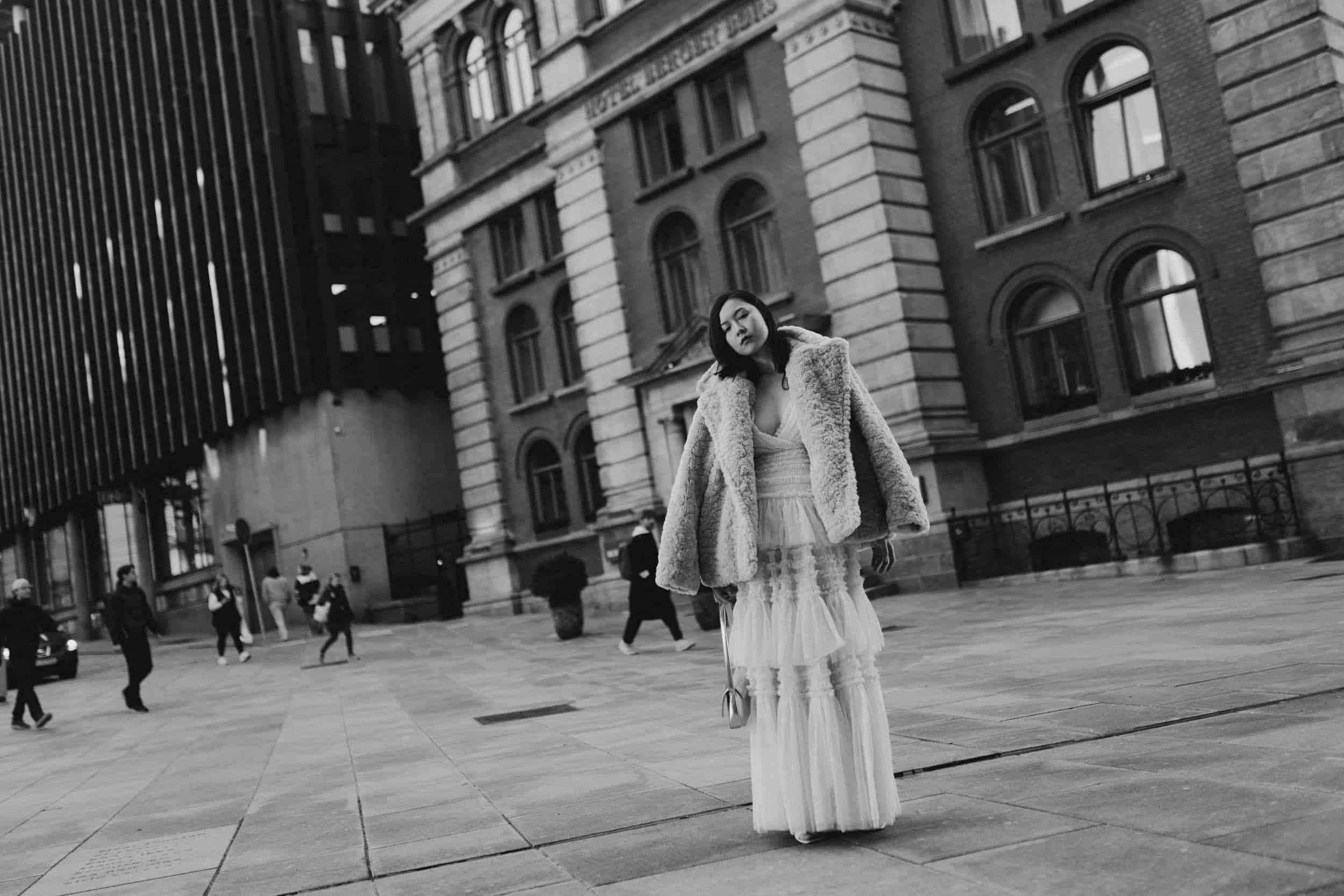 en kvinne i hvit kjole og pels som står på plaza