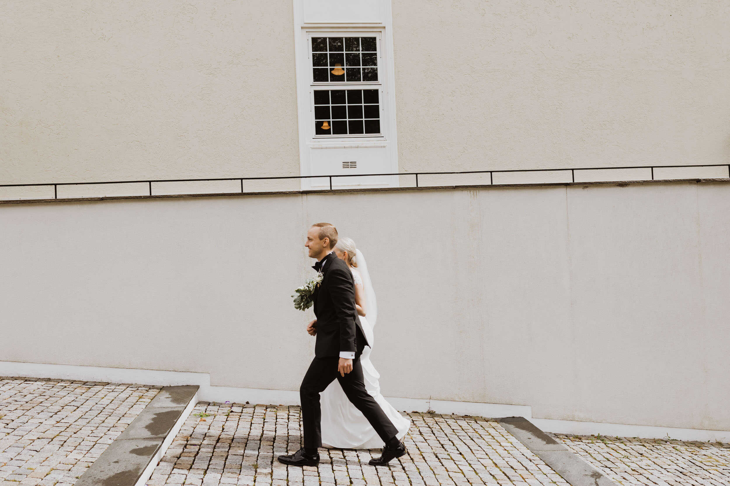 brudepar som går mot beige byggvegg