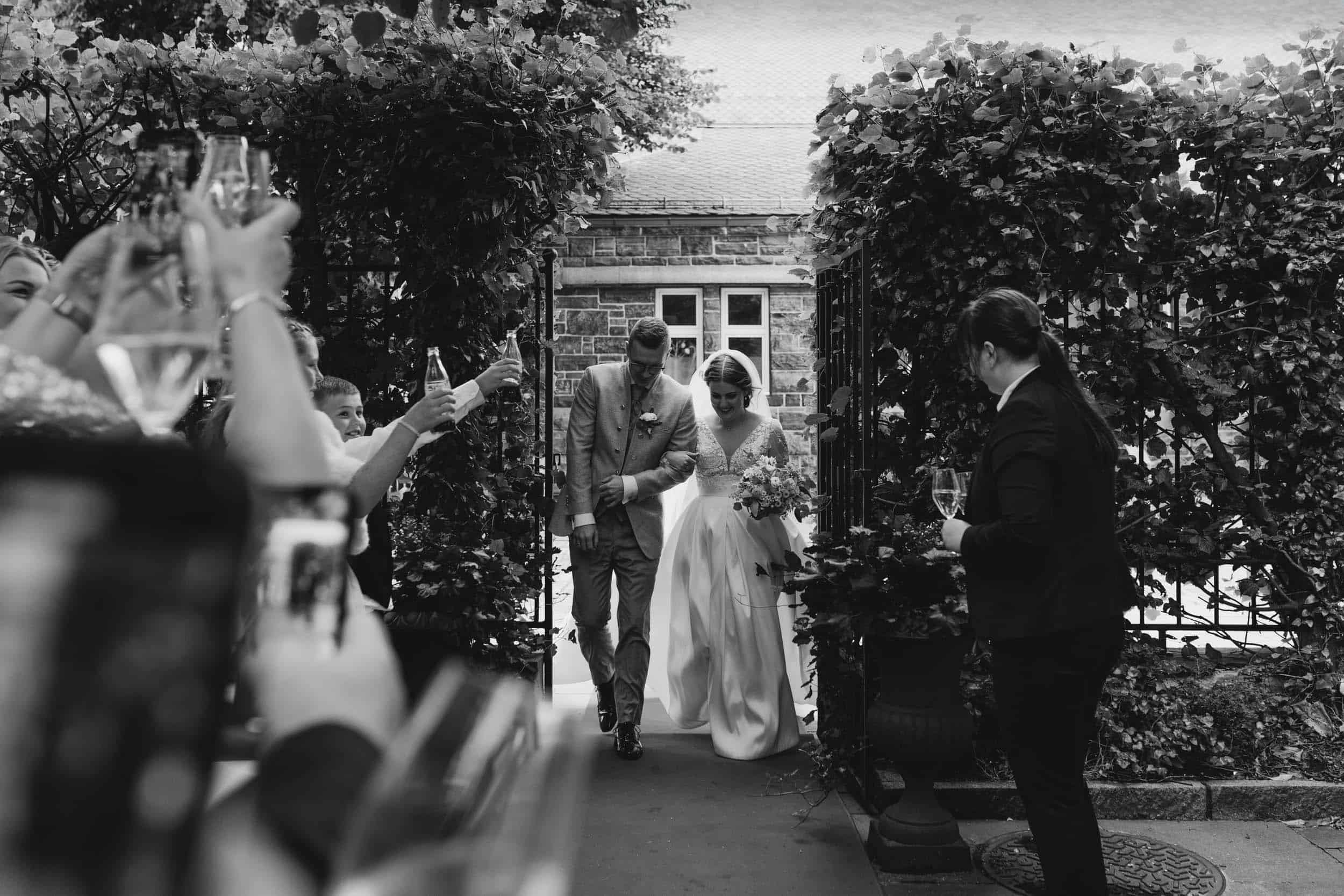 brudepar som går gjennom port og mennesker rundt dem som jubler