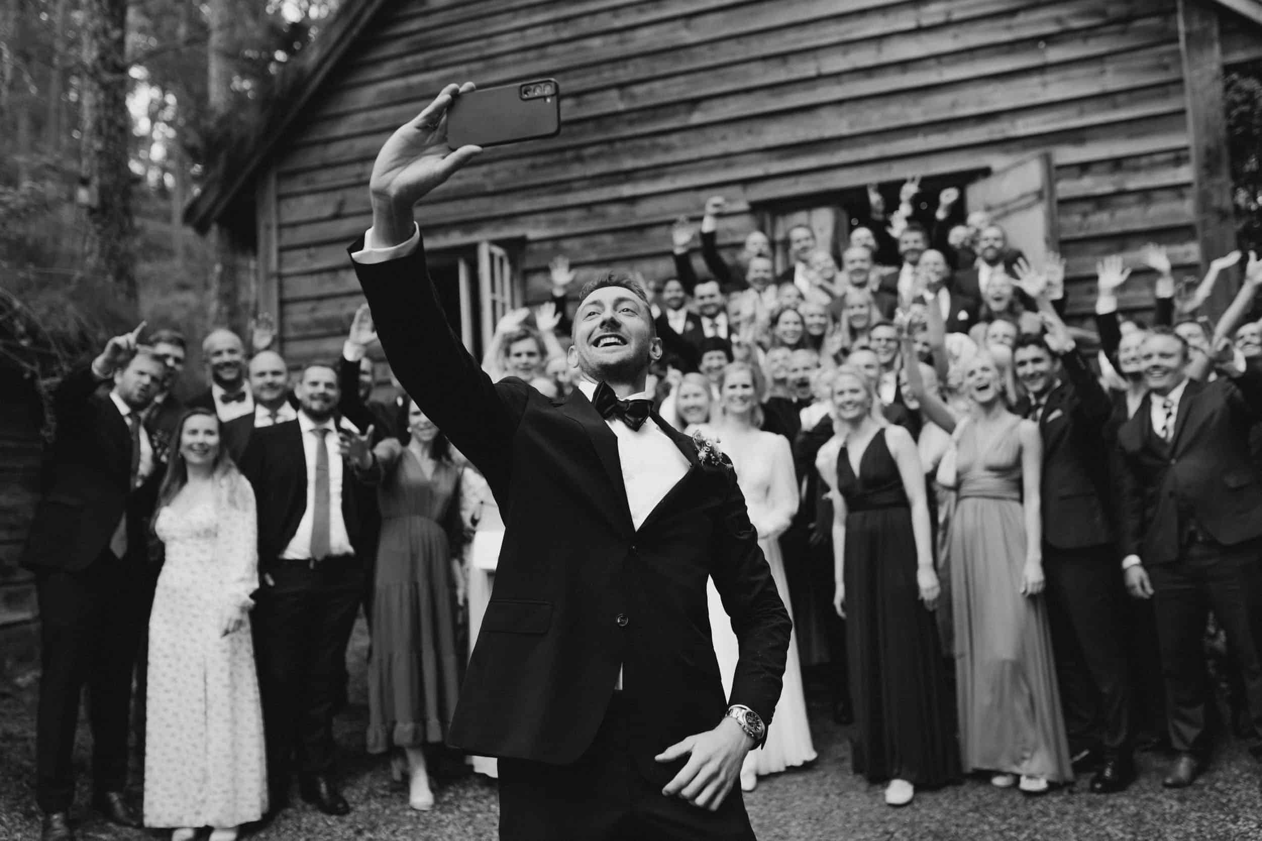 mann i dress tar selfie med mange mennesker bak han