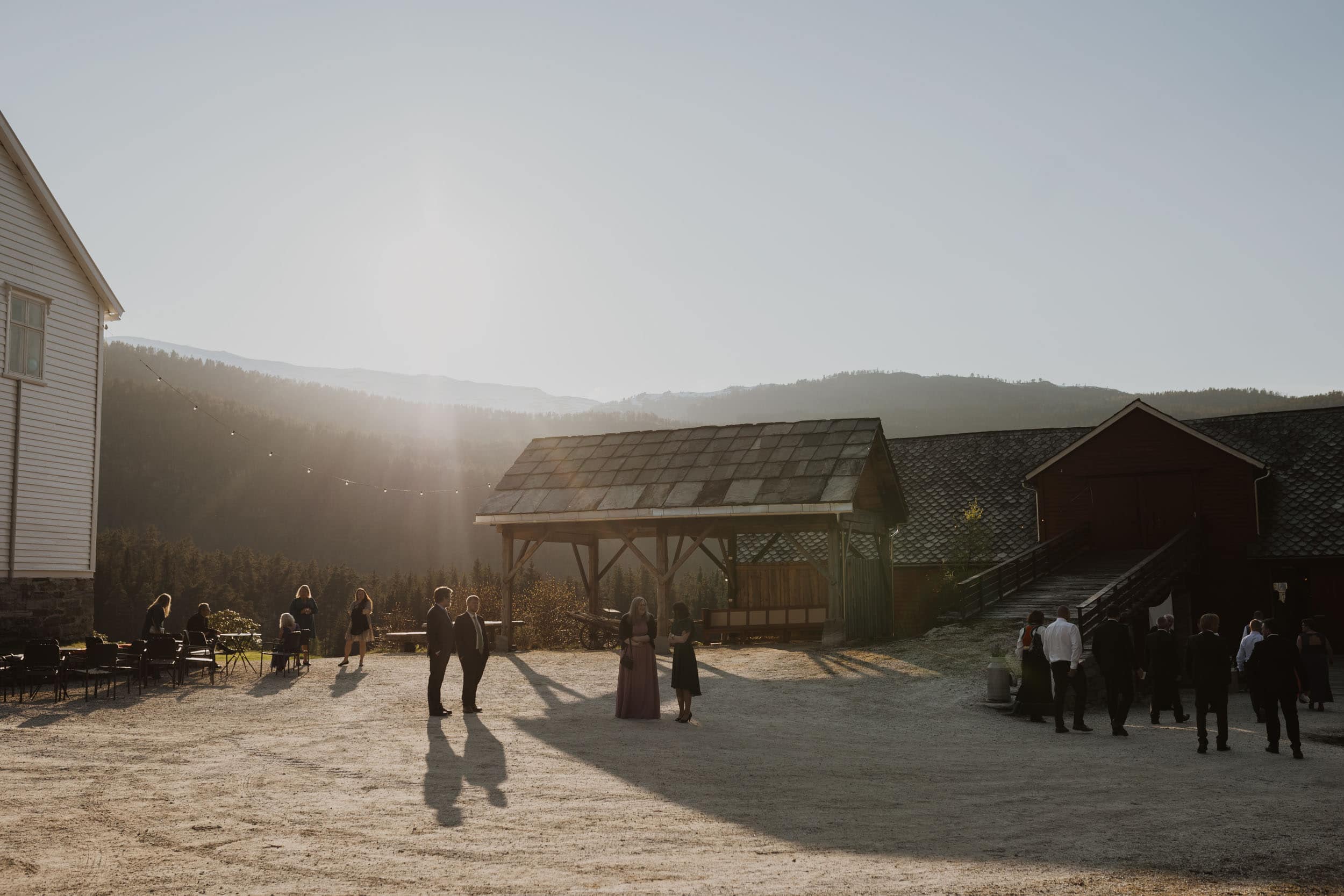 uteområde på en gård i solnedgangslys, med fjell, sol og låve