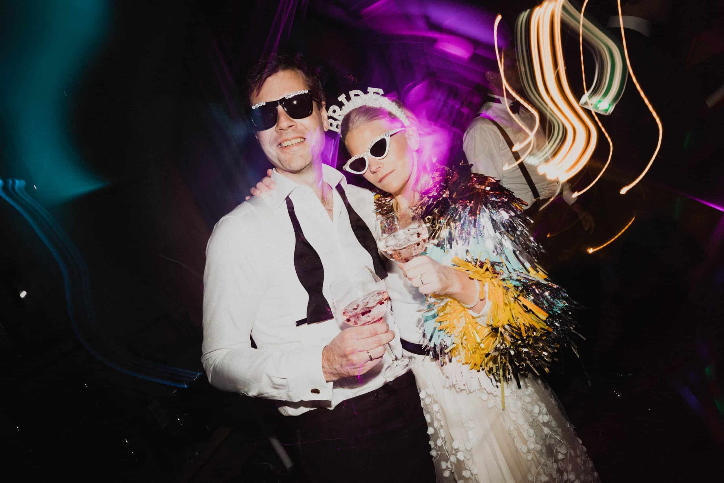 brudepar med solbriller på dansegulv poserer til bilde, masse lys rundt dem