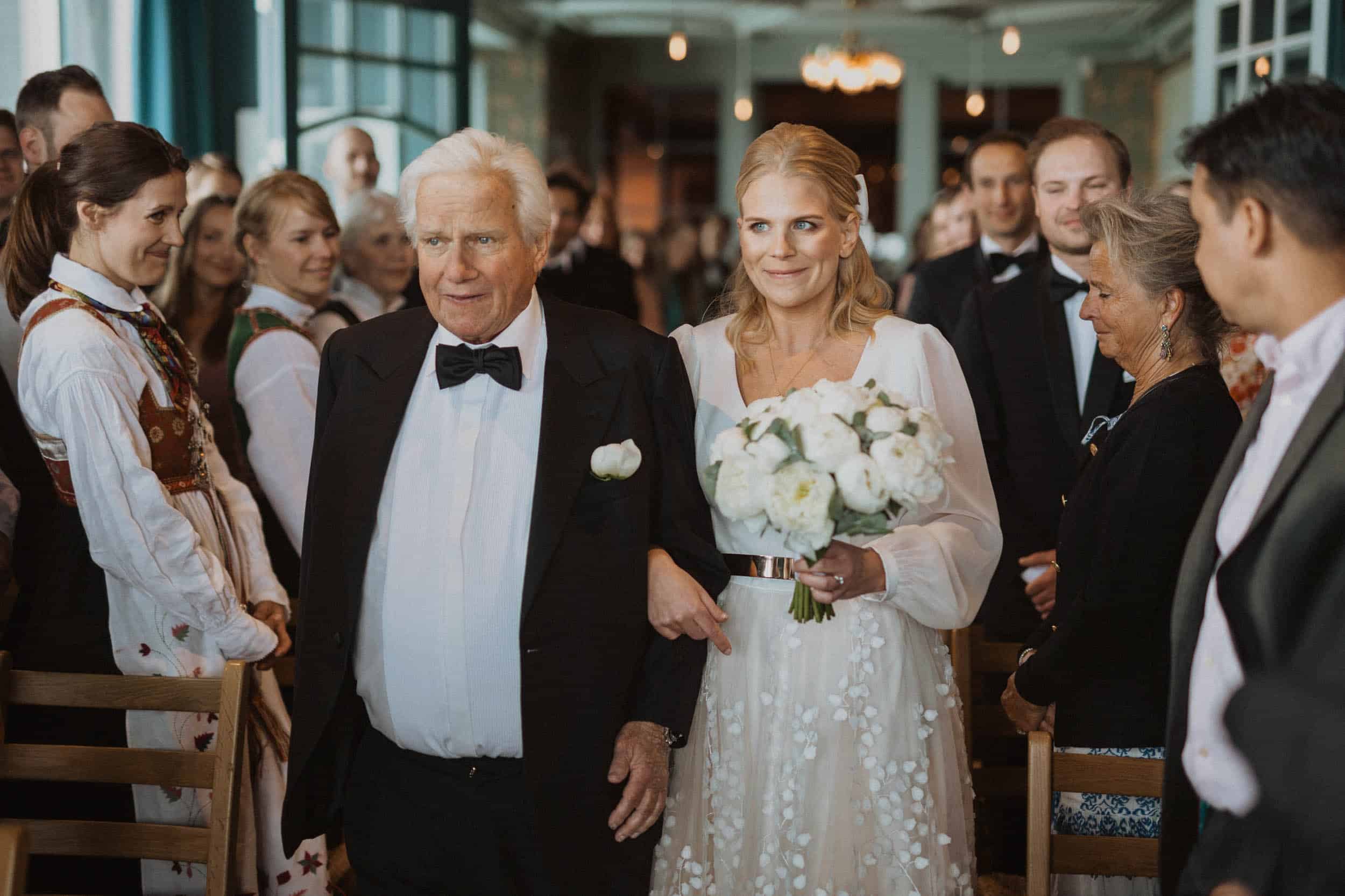 brud med blomsterbukett med sin far går mot alter, mennesker rundt dem