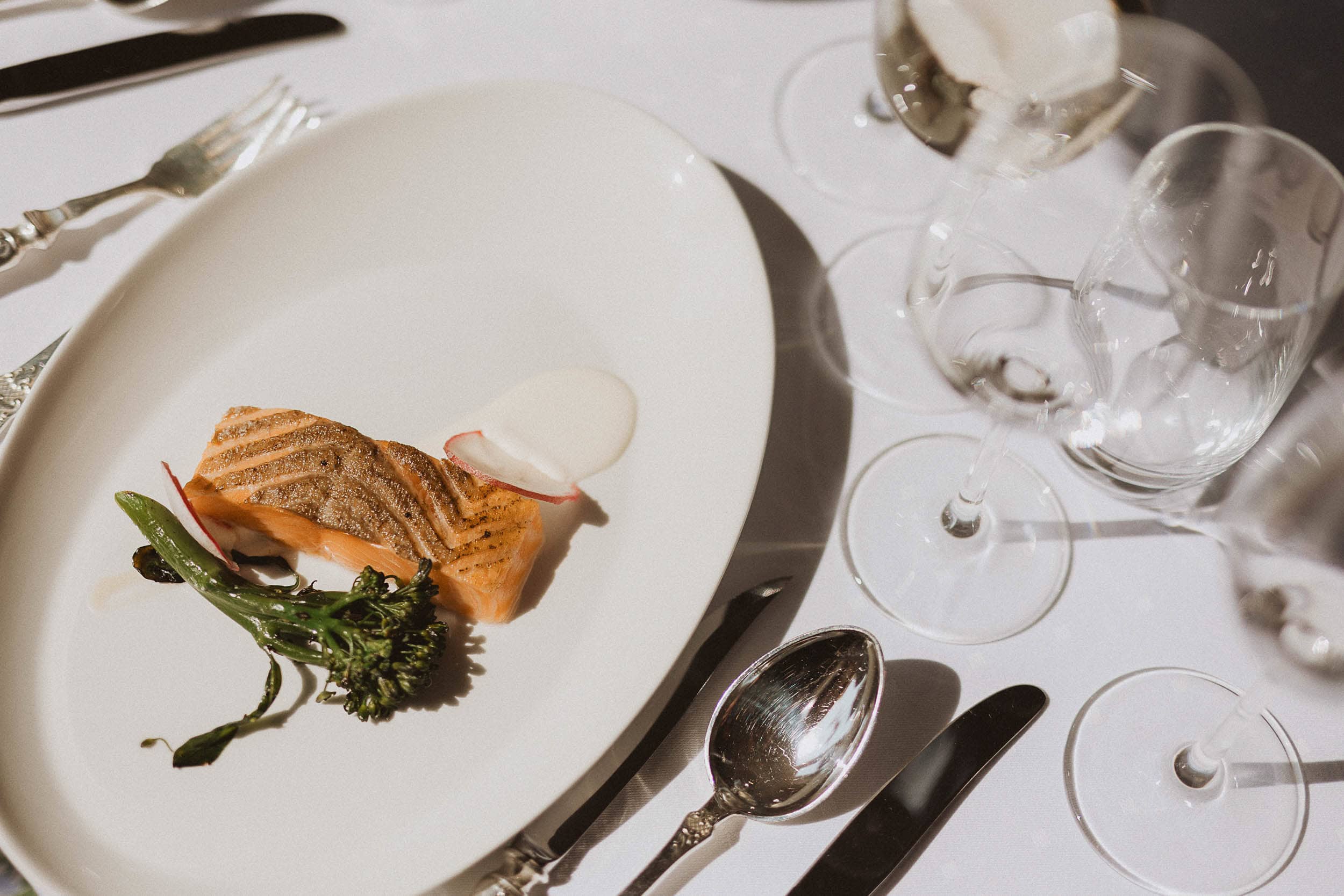 spisebord med fat med laks og brokkoli på, bestikk og et vinglass