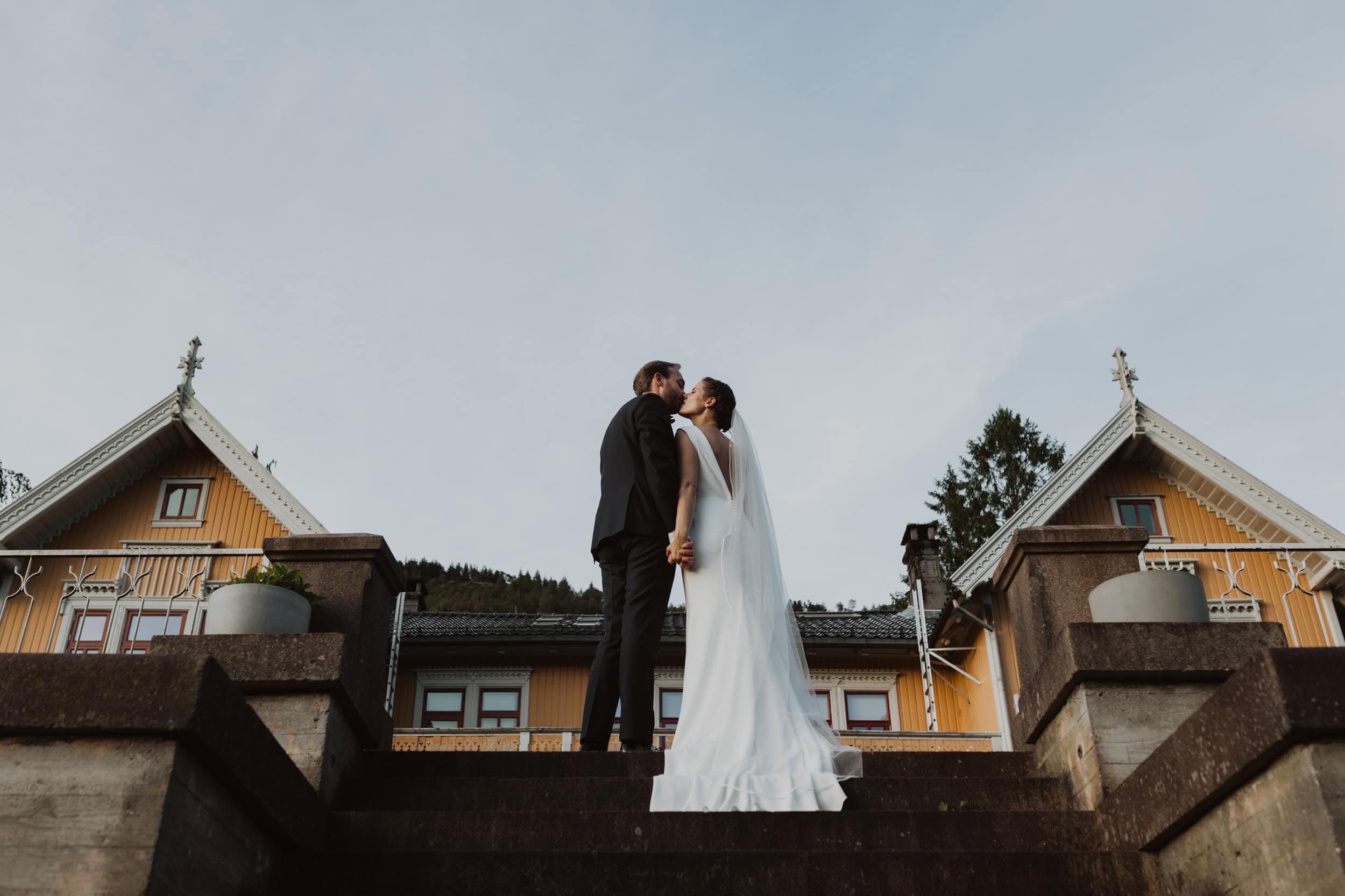 brudepar som kysser på trappene med et gult hus bak dem