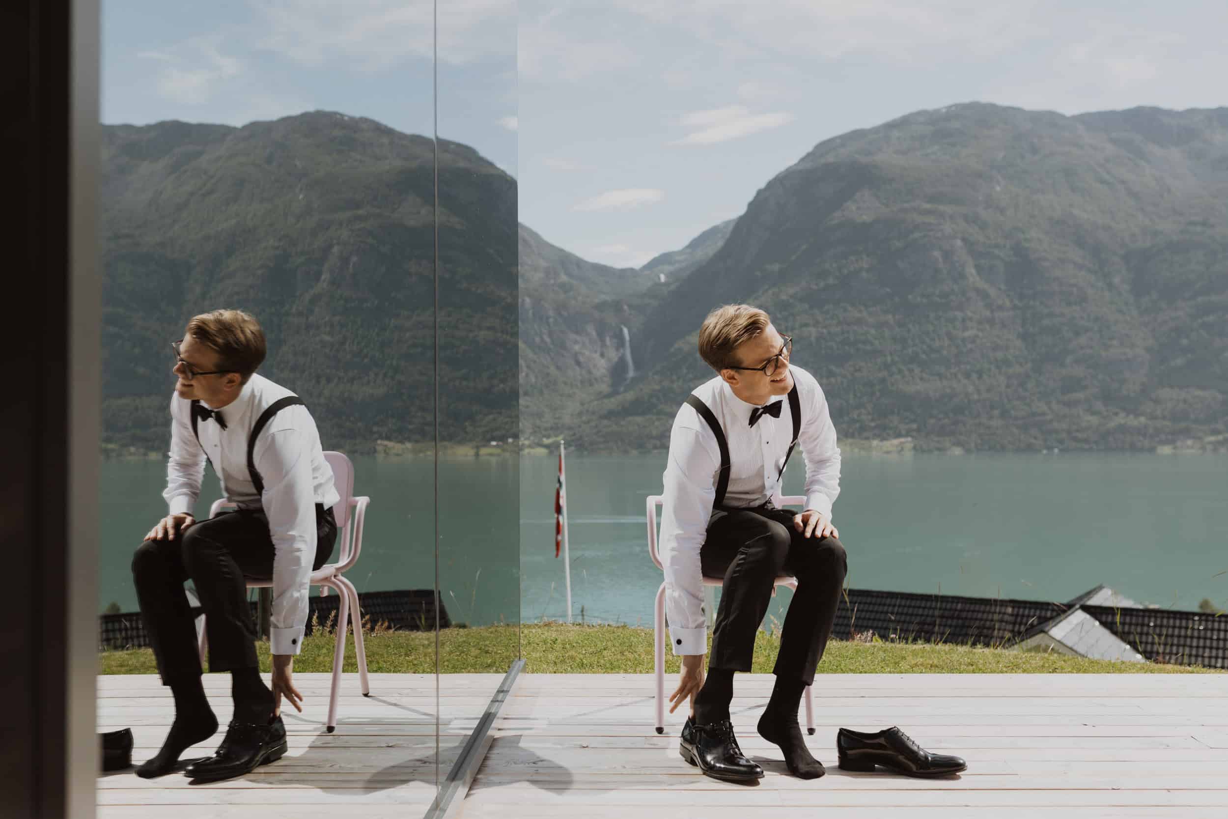 en mann i dress tar på sko, fjell og fjord bak han