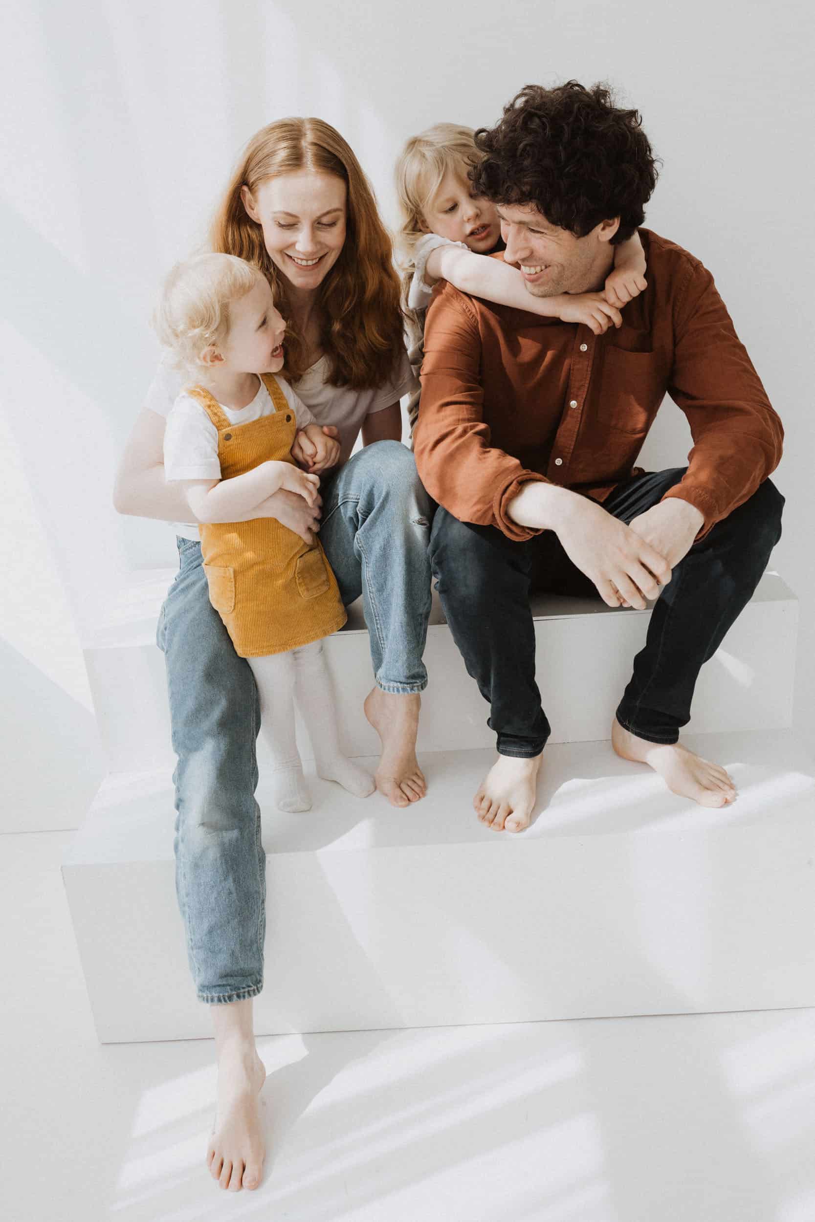 familie på fire i fargerike klær sitter mot en hvitt vegg